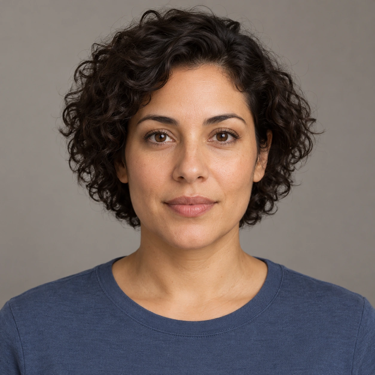 Original AI-generated fictional adult with short dark curls and a slate-blue shirt against a plain warm-gray background